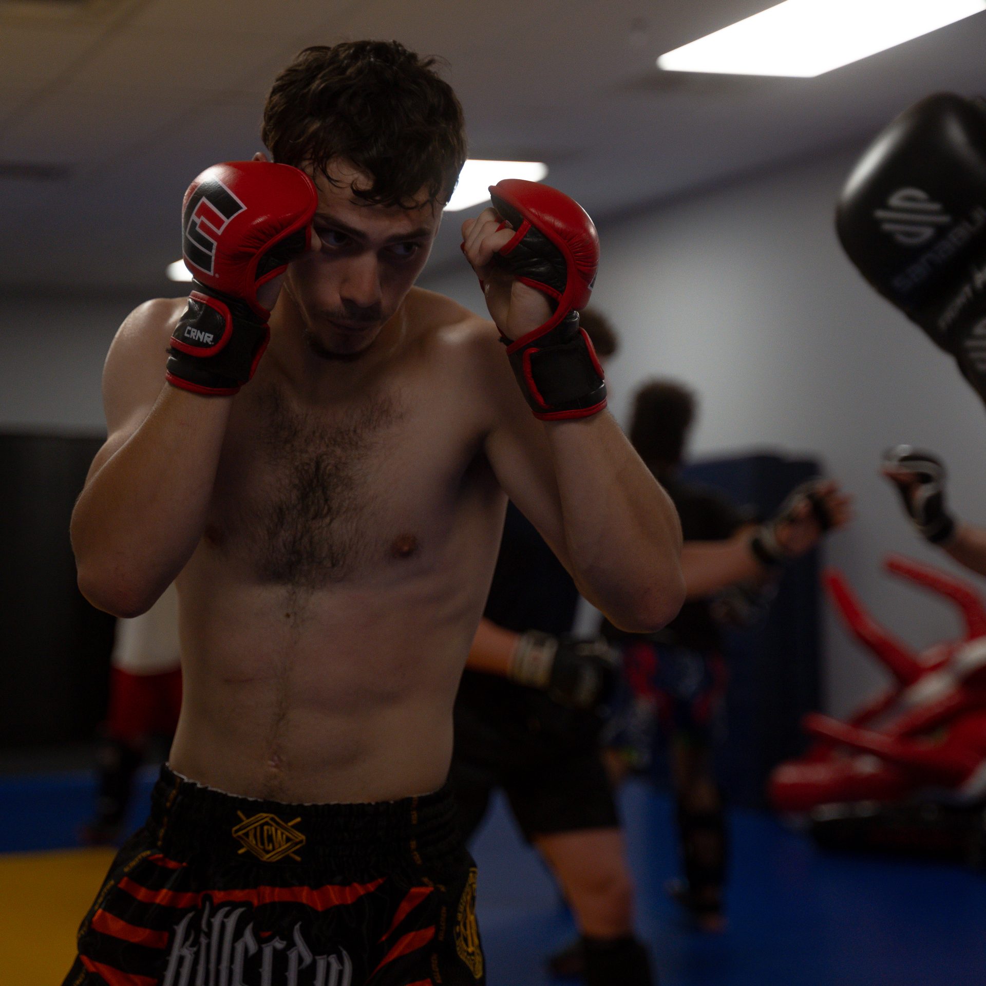 A fighter shadowboxing with a tight guard while class trains behind