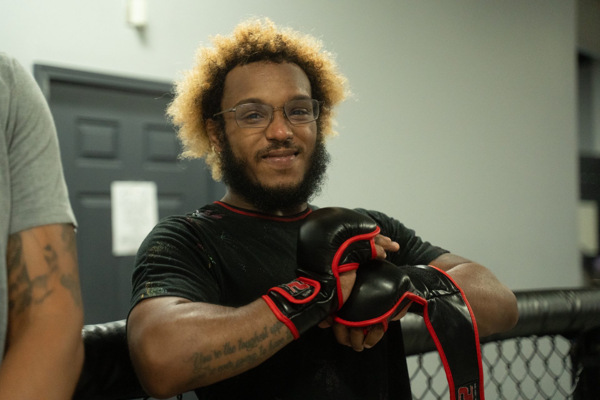 A smiling member gloving up at the cage before a round