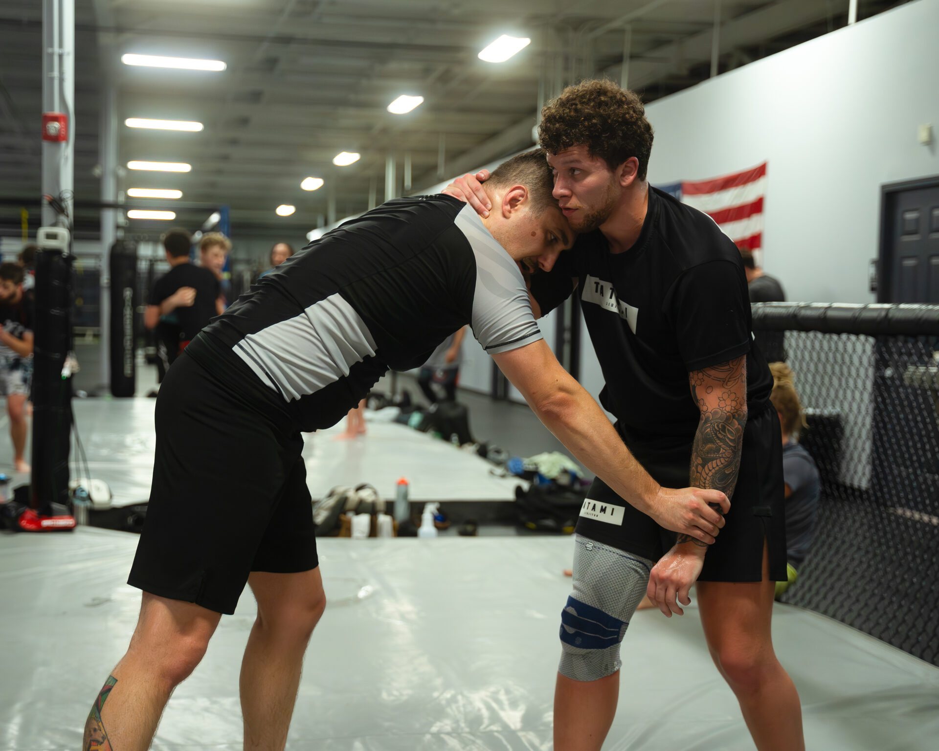 Two training partners in a standing collar tie in front of the cage