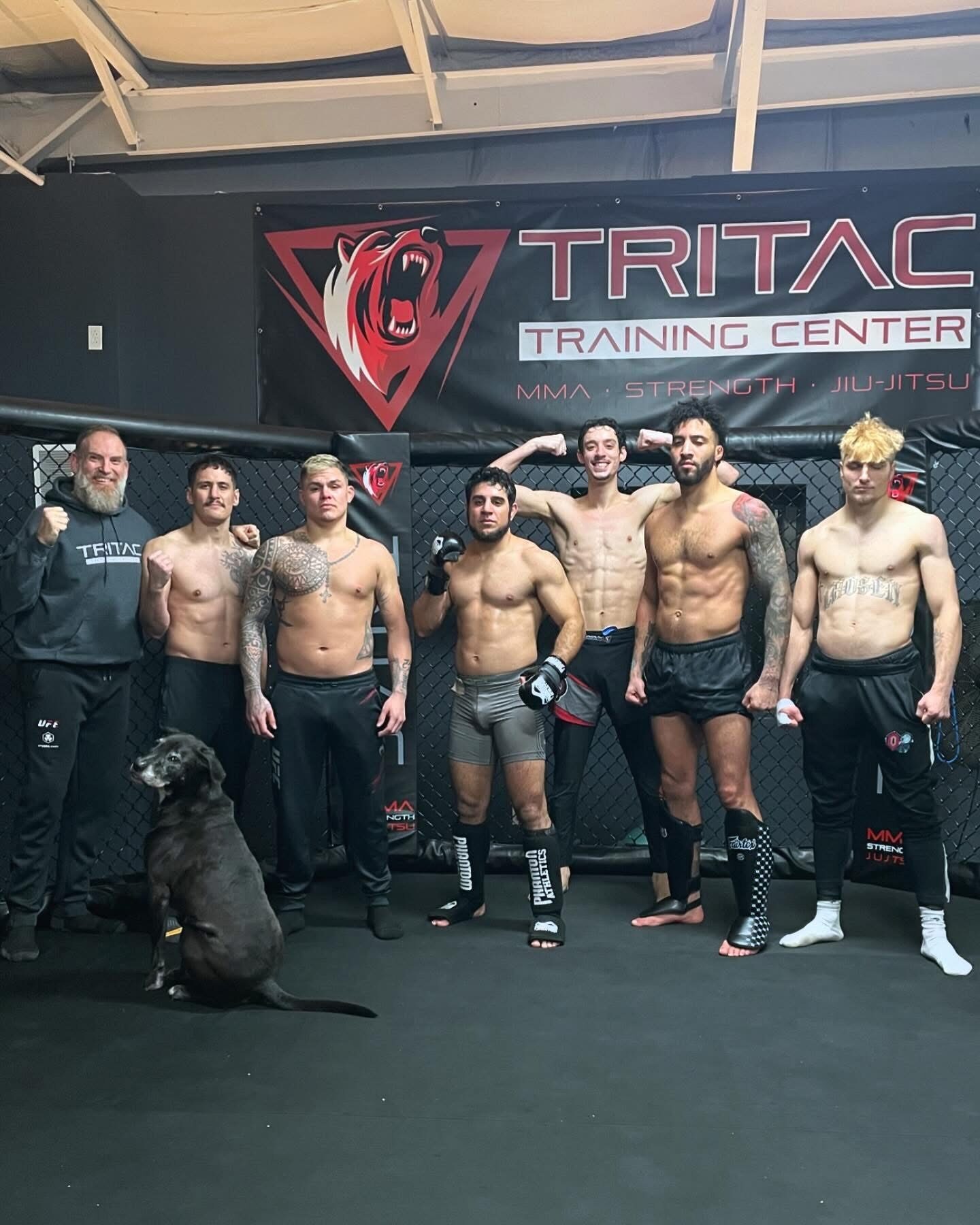 The TRITAC fight team lined up in front of the cage under the TRITAC Training Center banner