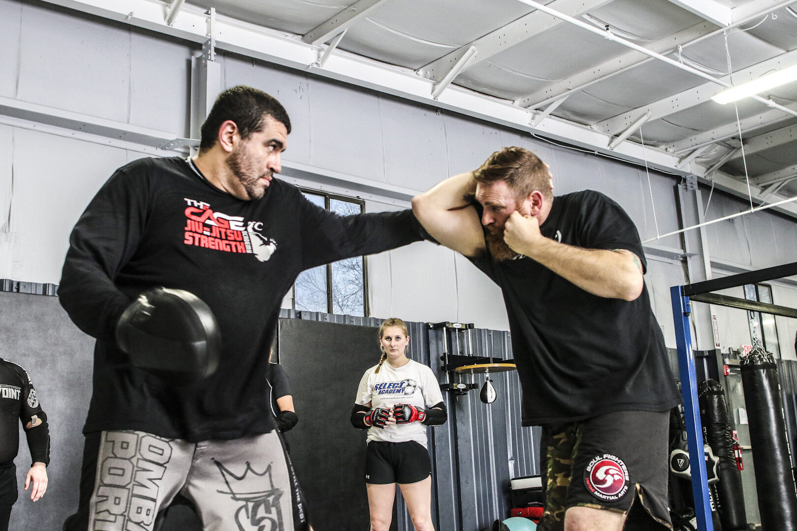 A punch landing on a covering guard during a gloved round while a third member watches from the side