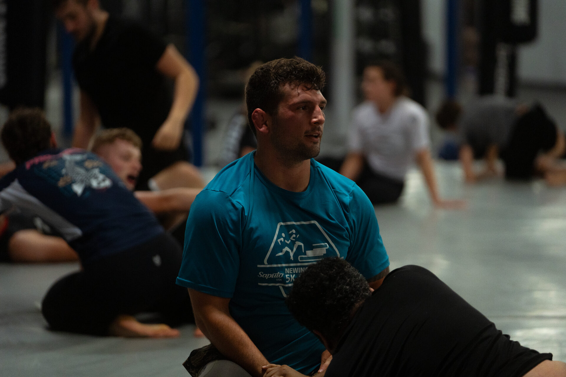 Pairs drilling on the ground across an open mat, one member in focus with his partner, no gym signage anywhere in the frame